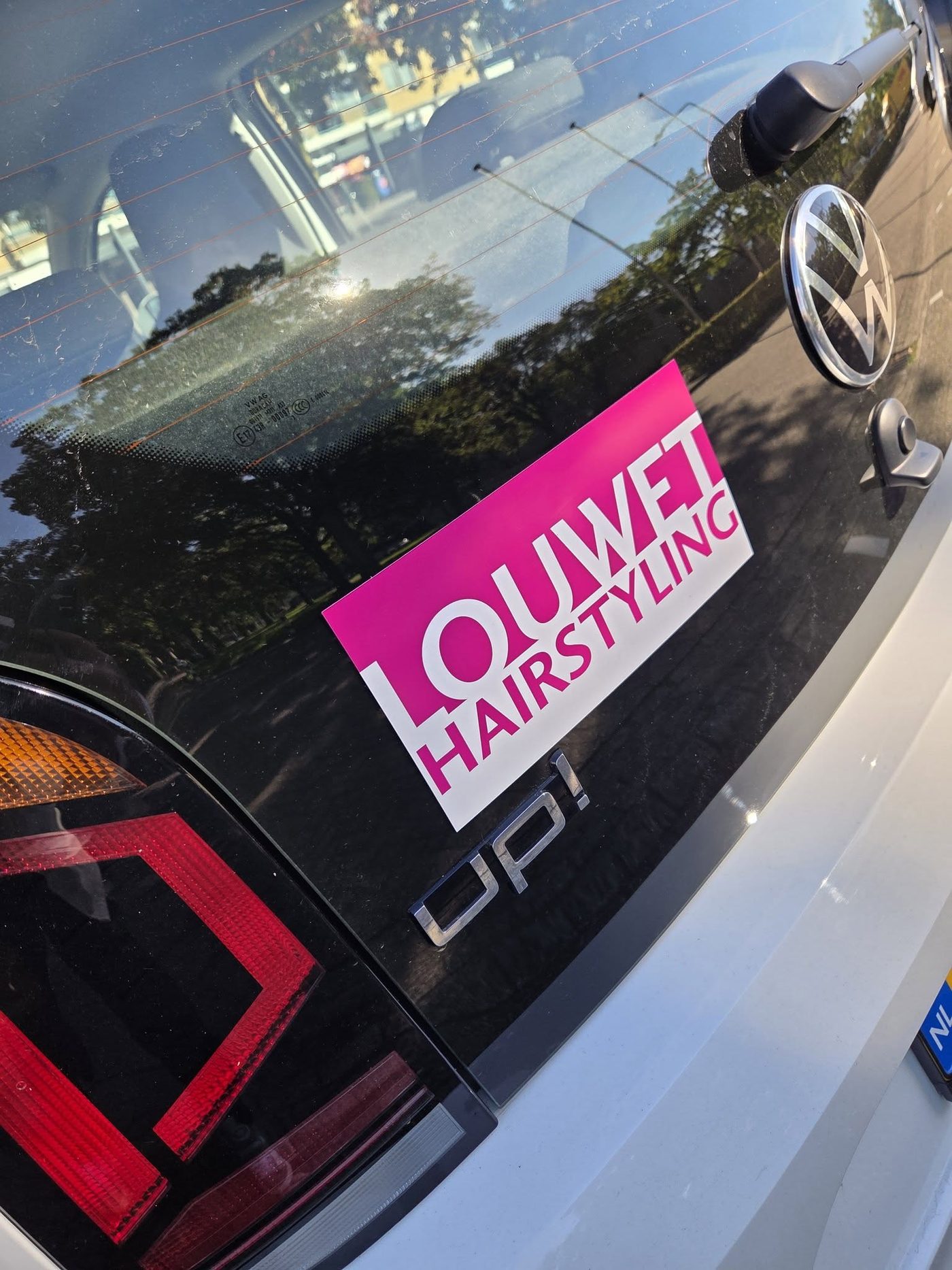 Achterkant van Saskia's zilverkleurige auto met de roze-witte sticker Louwet Hairstyling
